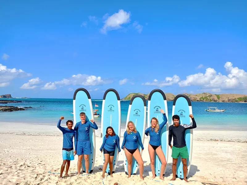 Happiness Surf Co instructors and students posing together on Selong Belanak Beach after successful beginner surf lesson in Kuta Lombok